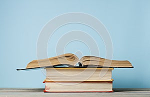 Open book, hardback books on wooden table and blue wall .Education background. Back to school. Copy space for text.