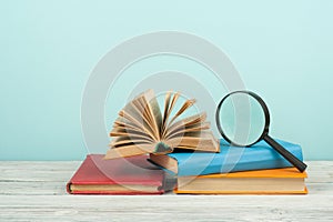 Open book, hardback colorful books on wooden table. Magnifier. Back to school. Copy space for text. Education business concept