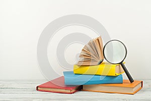 Open book, hardback colorful books on wooden table. Magnifier. Back to school. Copy space for text. Education business concept