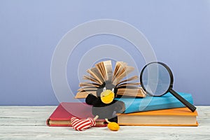 Open book, hardback colorful books on wooden table. Magnifier, toy crow. Back to school. Copy space for text. Education