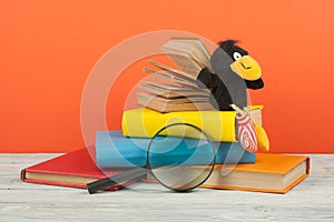 Open book, hardback colorful books on wooden table. Magnifier, toy crow. Back to school. Copy space for text. Education