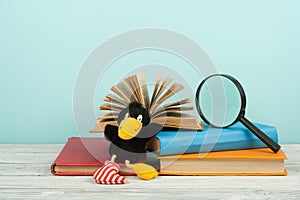 Open book, hardback colorful books on wooden table. Magnifier, toy crow. Back to school. Copy space for text. Education