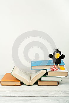Open book, hardback colorful books on wooden table. Toy crow. Back to school. Copy space for text. Education business