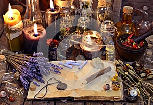 Open book with healing herbs, lavender flowers, candles, potion bottles and magic objects