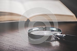 open book with magnifying glass on wooden desk in information library of school or university, concept for education,reading ,