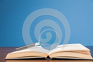 open book with magnifying glass on wooden desk in information library of school or university, concept for education,reading ,