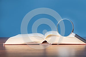 open book with magnifying glass on wooden desk in information library of school or university, concept for education,reading ,