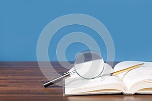 open book with magnifying glass on wooden desk in information library of school or university, concept for education,reading ,