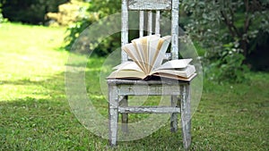 Open book on a old small chair on a green meadow in summer morning