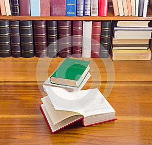 Open book and other books on wooden table and shelf