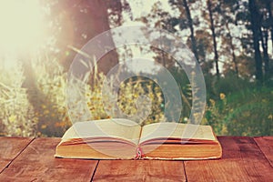 Open book over wooden rustic table in front of wild landscape and sunset light burst