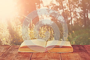 Open book over wooden rustic table in front of wild landscape and sunset light burst