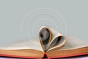 Open book pages curved into heart symbol and grey empty background