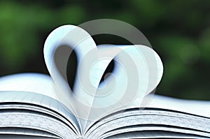 Open book with pages in heart shape on wooden table on nature