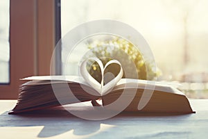 Open book with pages shaped as heart on wooden table