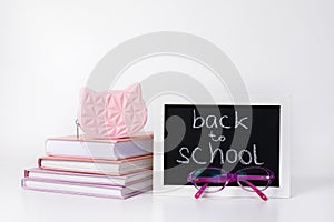 Open book, pile of books in pink and purple covers, glasses, pen, pencil, ruler abd blackboard frame on white background