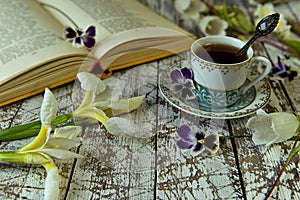 Open book of poetry, old cup of tea and flowers on table