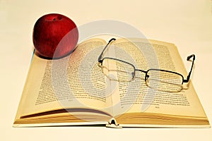 Open book, red apple and reading glasses on book pages