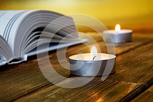 An open book of religious content lies on wooden boards against a golden background. Nearby are lit candles