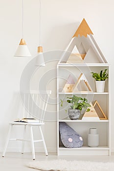 Open book on a simple, wooden chair and a bookcase with plants and DIY mountains decorations in a white, scandinavian living room