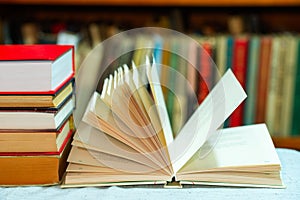 Open book, stack of hardback books on table. Top view.