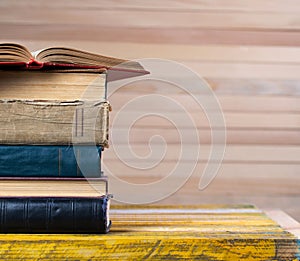 Open book, stack of hardback books on wooden table.