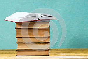 Open book, stack of hardback books on wooden table.