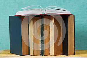 Open book, stack of hardback books on wooden table.