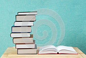 Open book, stack of hardback books on wooden table.