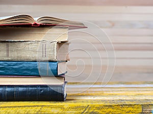 Open book, stack of hardback books on wooden table.