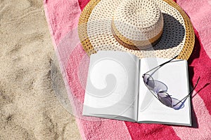 Open book, sunglasses, hat and striped towel on sandy beach, above view. Space for text