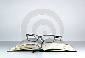 Open book on the table inviting you to read. Reading glasses on the book.