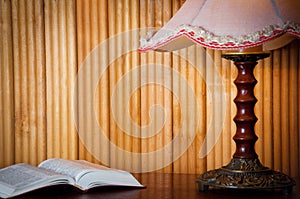 Open book on table and old vintage lamp on wooden background at home in the evening. Horizontal photo. Space for text.