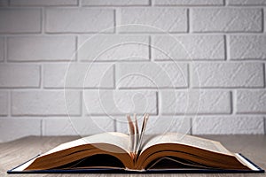 An open book with torn pages on a table against a wall of white decorative bricks.