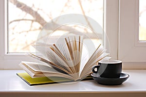 An open book on the window and a coffee cup