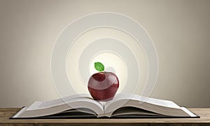 Open book on a wooden Desk with a red Apple