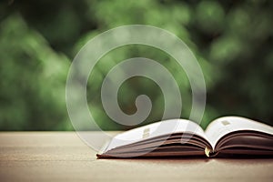 Open book on a wooden shelf with beautiful nature background