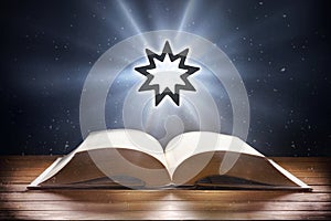 Open book on wooden table and bahai symbol front view