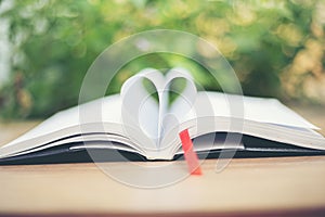 Open book on wooden table on natural background. Heart book page