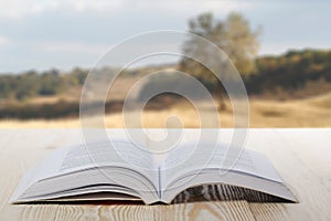 Open book on wooden table on natural blurred background