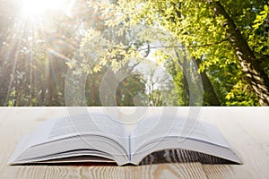 Open book on wooden table on natural blurred background