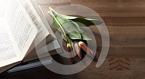 An open book on a wooden tray. Flowers on the book. A stack of books. Workplace.