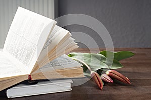 An open book on a wooden tray. Flowers on the book. A stack of books. Workplace.