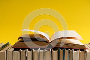 Open book on yellow background, hardback books on wooden table.
