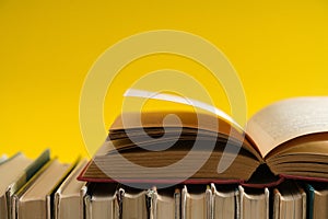 Open book on yellow background, hardback books on wooden table.