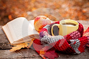 Open book and yellow tea mug with warm scarf and apple