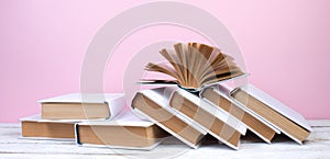 Open books, hardback colorful books on wooden table. pink background. Back to school. Copy space for text. Education business