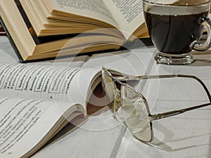 Open books with reading glasses, cup of coffee on the table