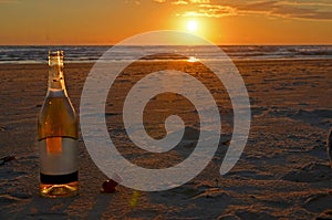 An open bottle of champagne stands with a cork stopper on the sand. Meeting of the sunset on the Mediterranean Sea in Israel.