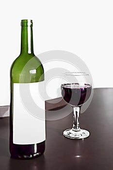 Open bottle and one glass of red wine on brown wodden table and white blurred wall background. Alcohol drink on desk in room. Mock